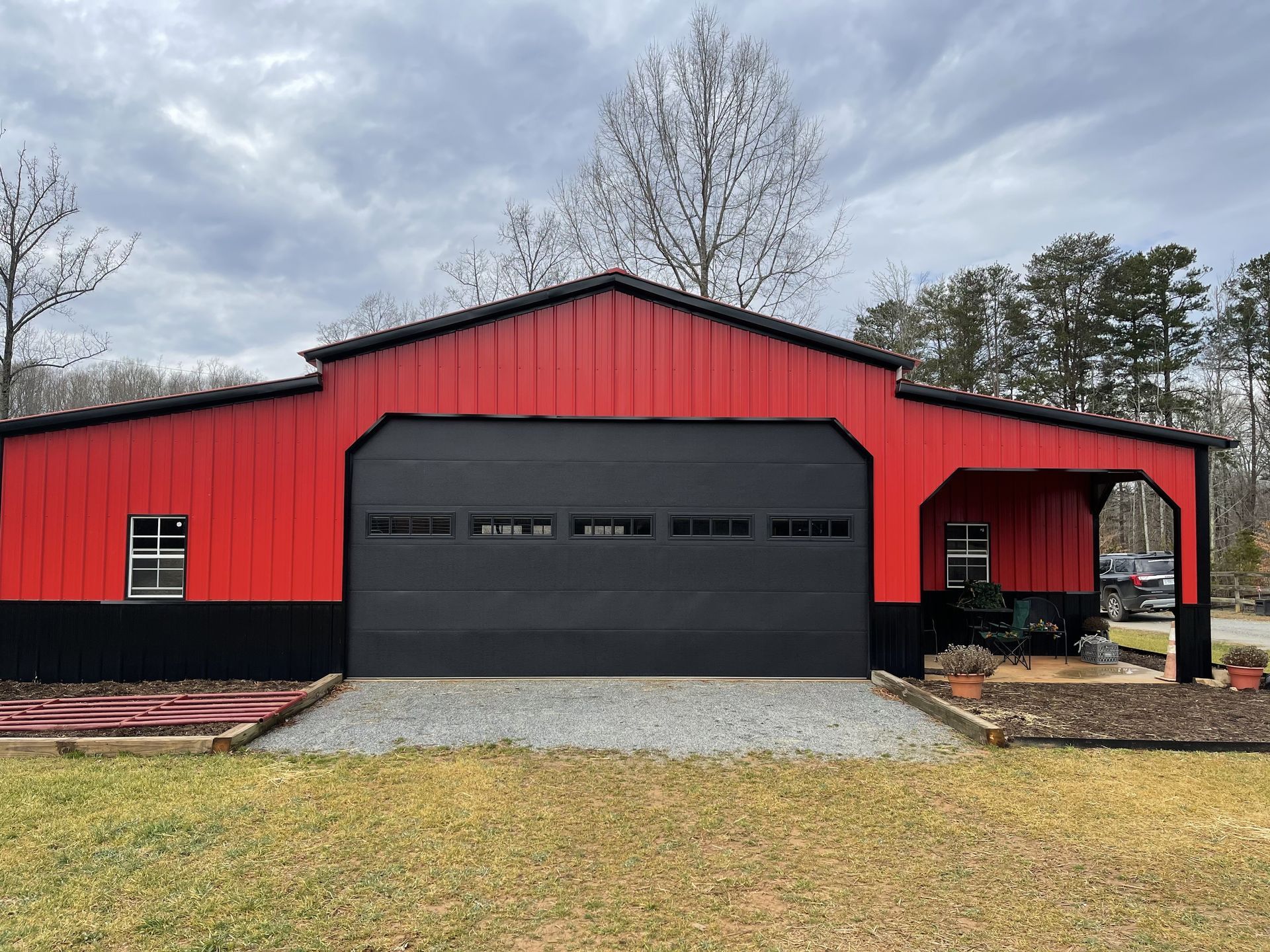 Red and black barn-style garage with a black garage door and gravel driveway under a cloudy sky.