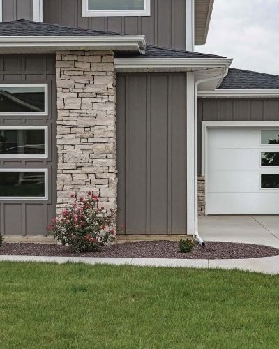 Exterior of a modern house with stone and gray siding, white garage door, and lush green lawn.