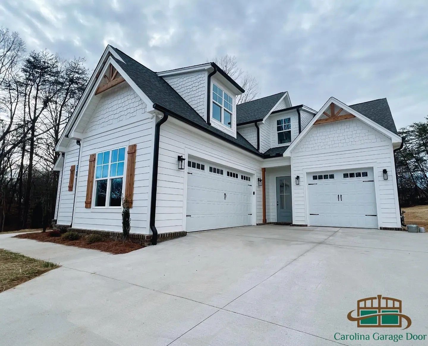 White house with black roof, three-car garage. Brown wood accents on gables and shutters. Cloudy sky.