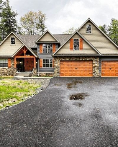 House with stone and wood siding, orange garage doors, and a dark asphalt driveway.