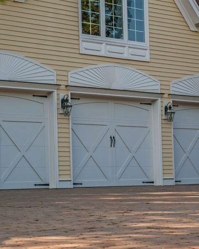 Three white garage doors with arched tops, lights, and a window above. Yellow siding.