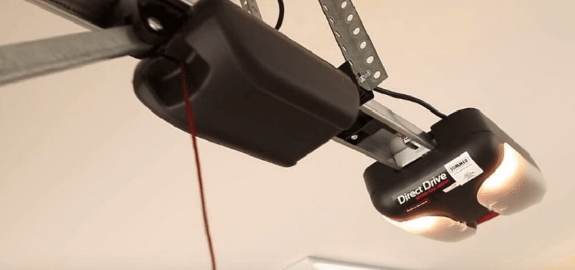 Garage door opener. Black and gray mechanism attached to the ceiling. Lights are on.