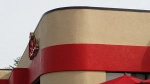 A close-up of a Chick-fil-A building exterior with curved tan walls and a horizontal red stripe.