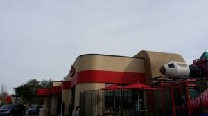 A McDonald's restaurant exterior with a tan and red facade and a decorative rocket ship structure on the playground.