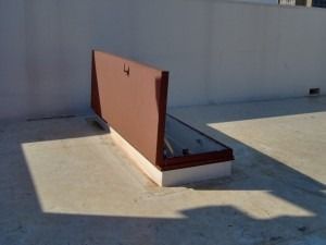 A brown, rectangular roof access hatch open on a flat, light-colored roof.
