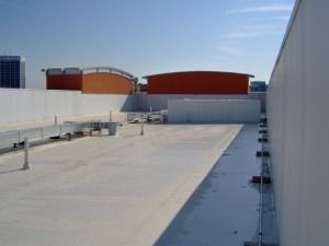 A flat rooftop with white surfaces, metal ductwork, and orange curved structures in the distance under a clear blue sky.