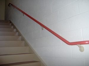 A bright red handrail runs along a white cinder block wall next to a concrete staircase.
