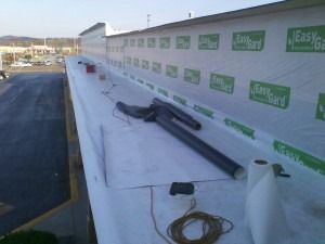 Construction materials, including rolled membrane and tools, sit on a building rooftop with EasyGard barrier on the wall.