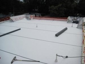 A flat rooftop under construction featuring white waterproof membrane, construction tools, and insulation rolls.