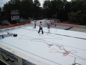 Workers install a white, flat roofing membrane on a commercial building rooftop.