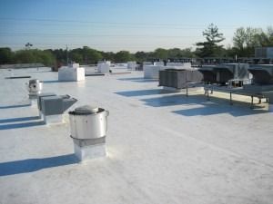 A white, flat commercial roof featuring multiple ventilation units and HVAC equipment under a clear blue sky.
