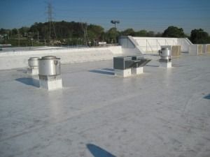 A white commercial rooftop with several metallic ventilation fans and equipment curbs under a clear blue sky.