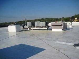 A flat white commercial roof featuring several HVAC units under a clear blue sky.