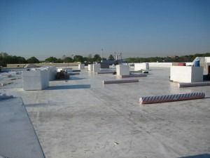 A flat, white commercial roof under a clear blue sky, with scattered construction materials and blocks.