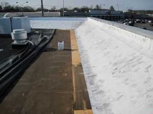 A flat roof showing a transition between an old black surface, a strip of wood, and a newly applied white coating.