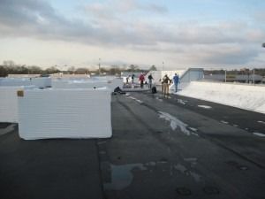 A group of workers on a flat roof surrounded by large, white rectangular construction blocks under a cloudy sky.