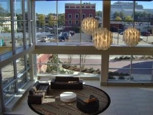 A high-angle view of a modern building lobby with floor-to-ceiling windows, sculptural pendant lights, and a lounge area.