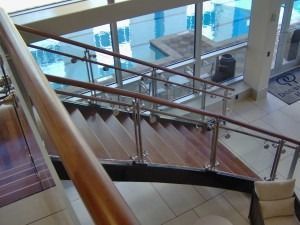 A wooden staircase with metal handrails leading down toward a view of an indoor swimming pool.