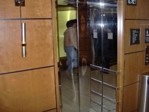 A person standing in front of a mirrored elevator door with wooden paneling on the walls.