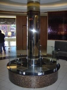 A circular granite platform with a central metal pillar surrounded by a glass railing in a modern indoor lobby.