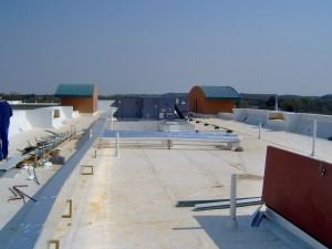 A wide-angle view of a flat, light-colored roof with mechanical units, vents, and a person standing on the left.