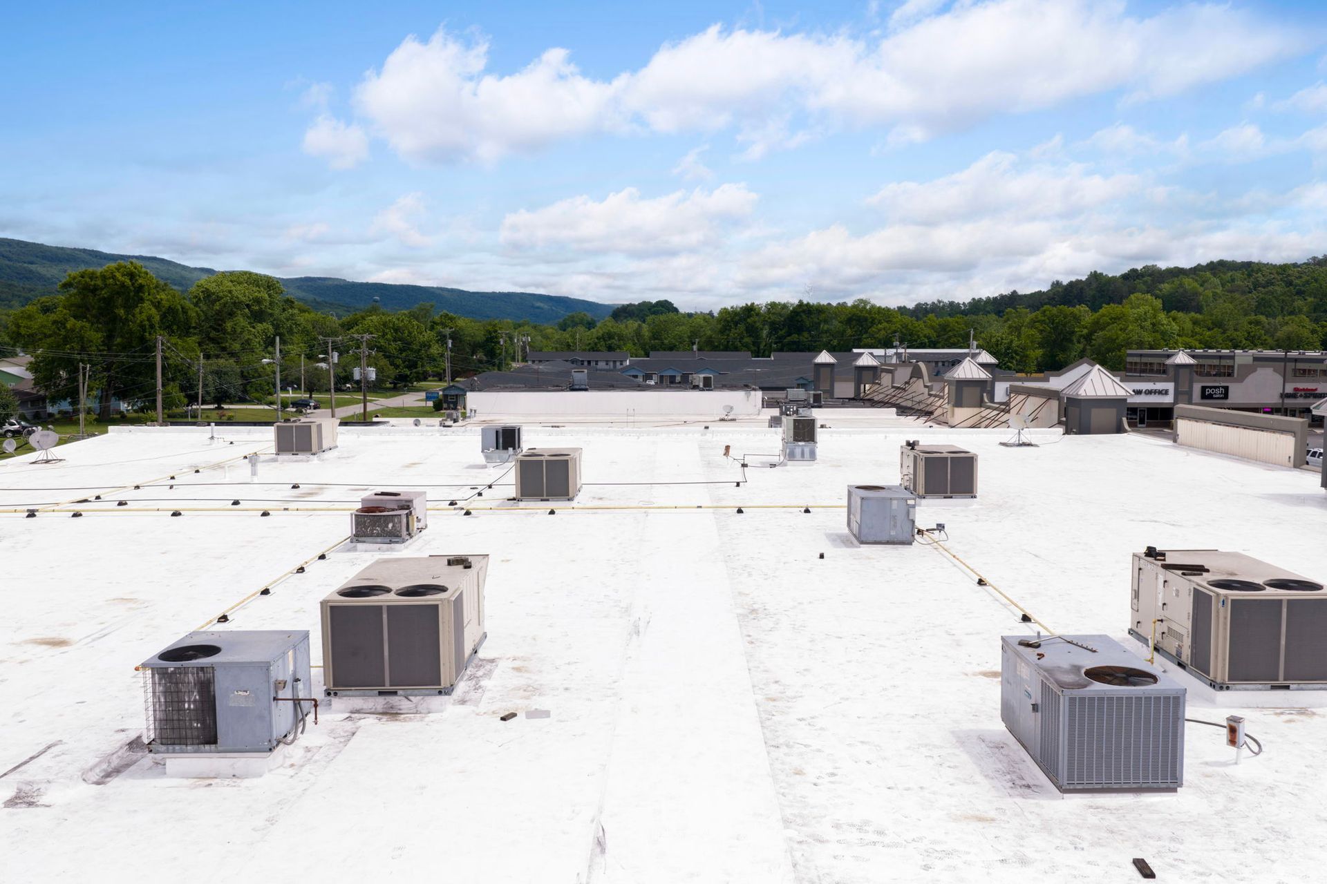 Rooftop with multiple HVAC units under a blue sky, overlooking green hills and trees