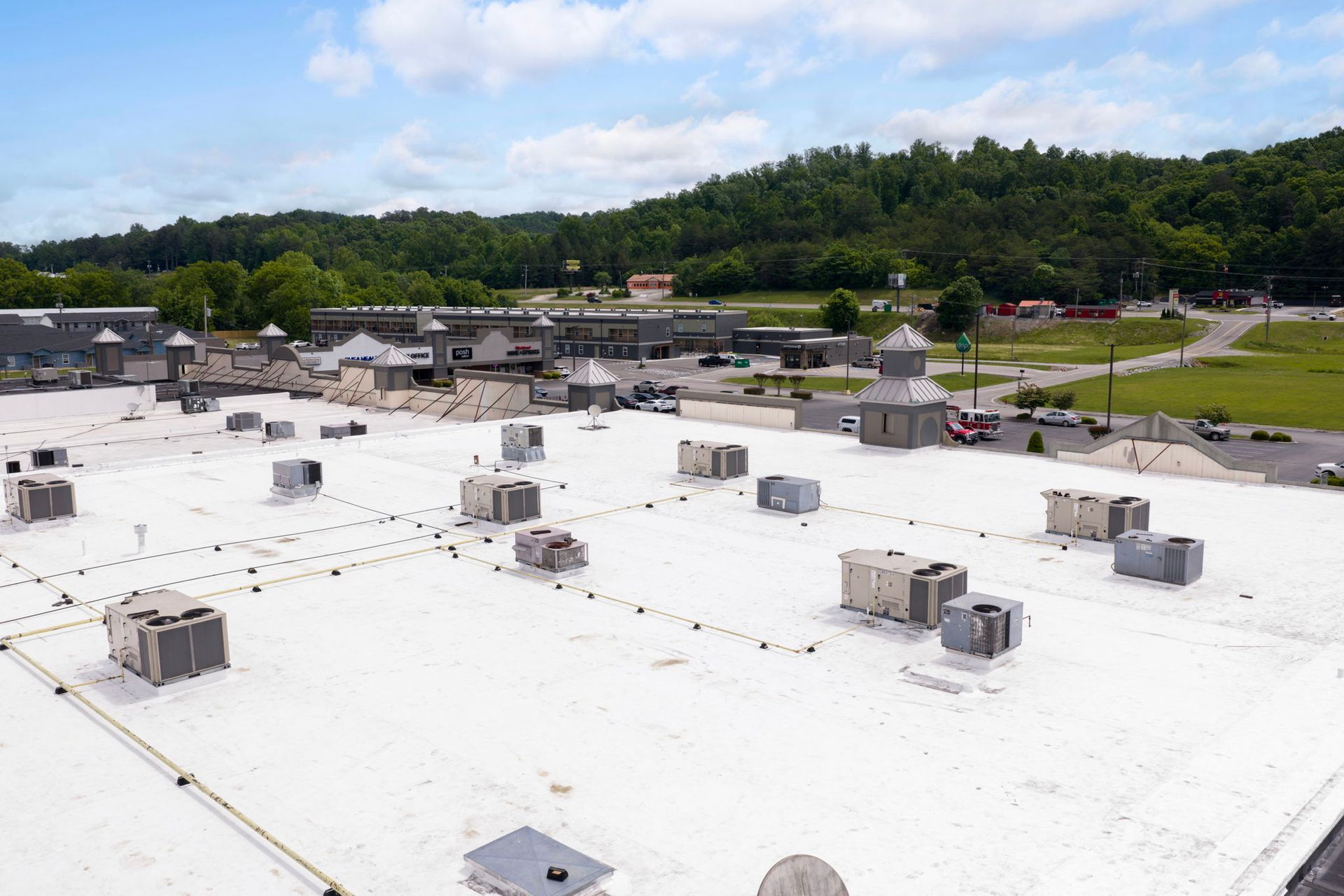 Rooftop HVAC units on a white industrial building with green hills and a partly cloudy sky in the background