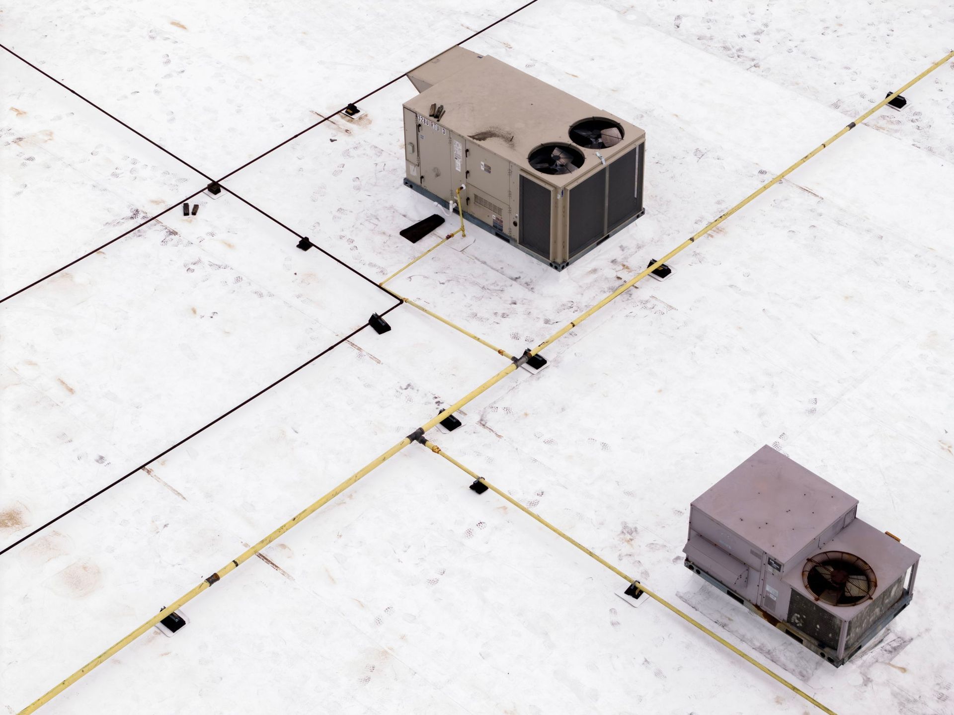 Two rooftop HVAC units on a white membrane roof with seams and yellow guide lines