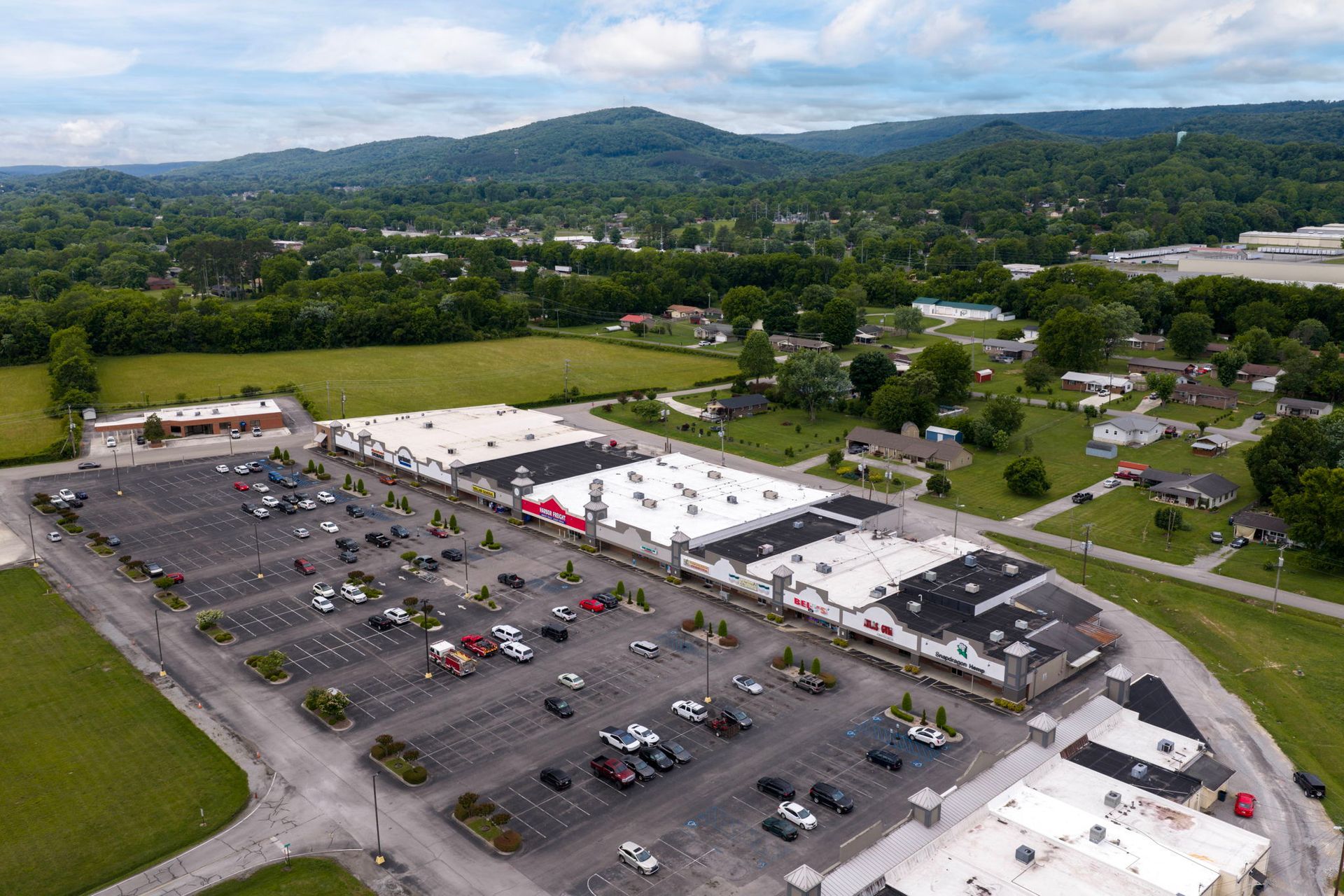 Aerial view of a large parking lot and shopping center with surrounding green fields and hills.