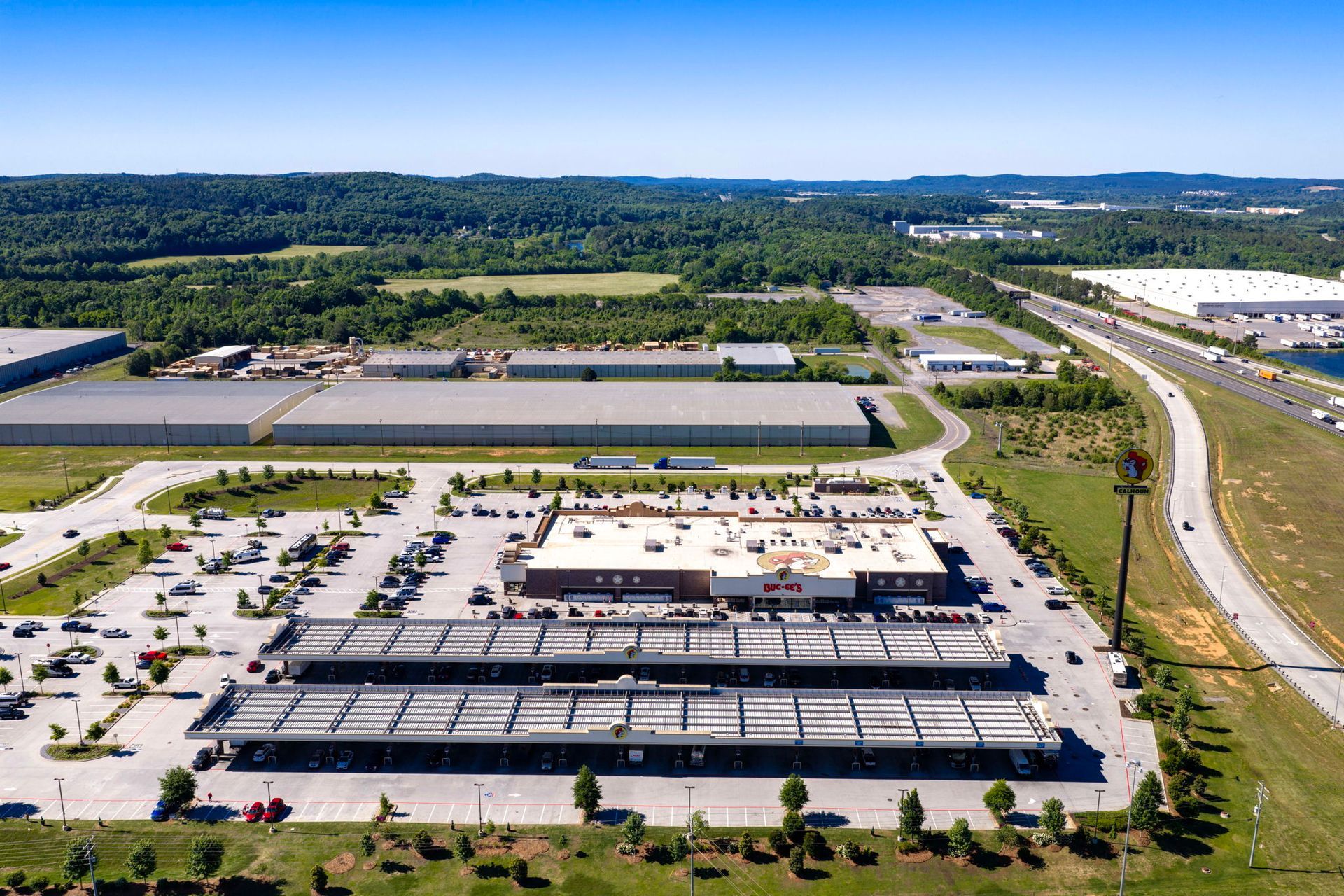 Aerial view of a large warehouse complex with parking lots, roads, and surrounding green fields
