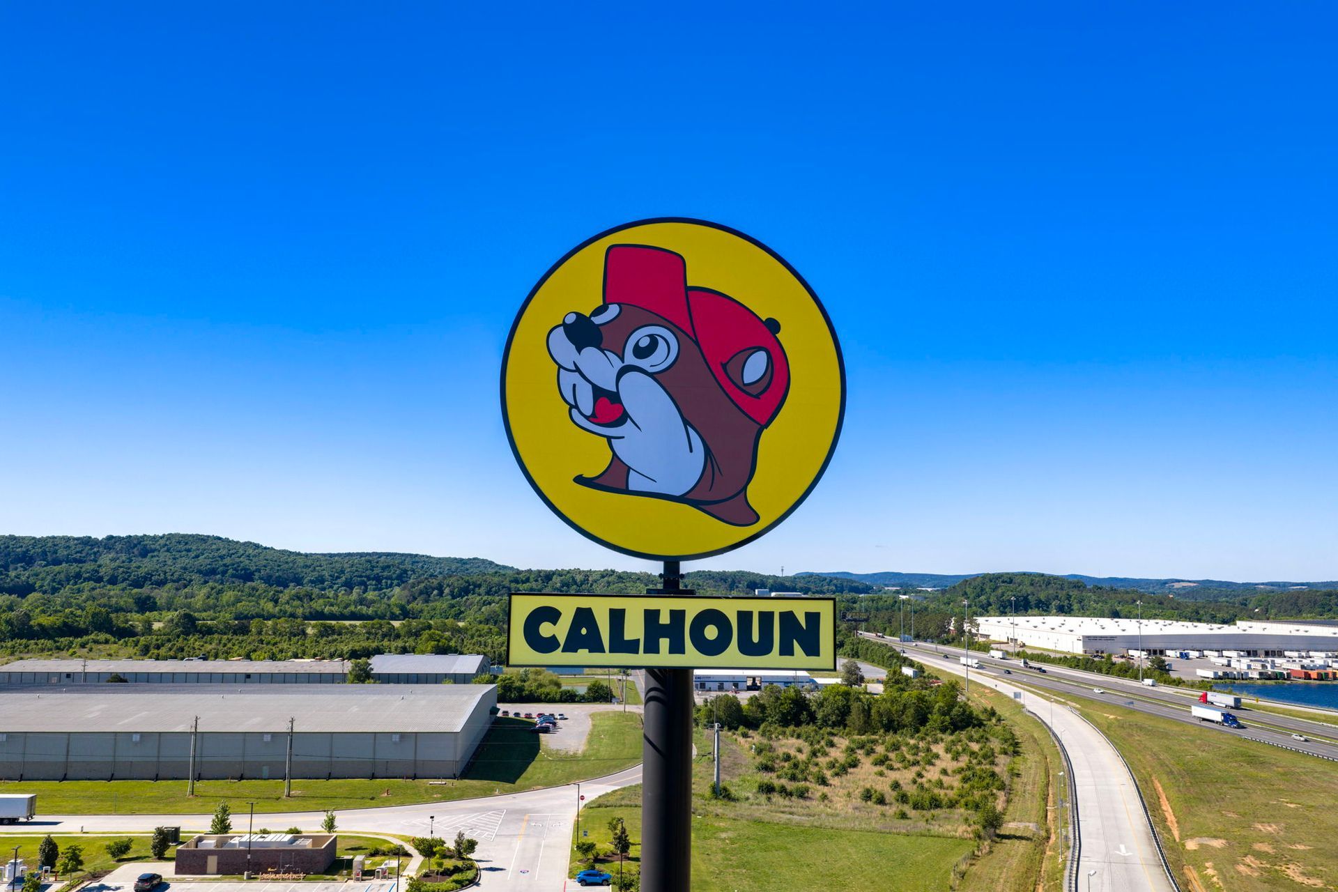 Calhoun roadside sign with a cartoon beaver on a yellow circle above a highway and river landscape