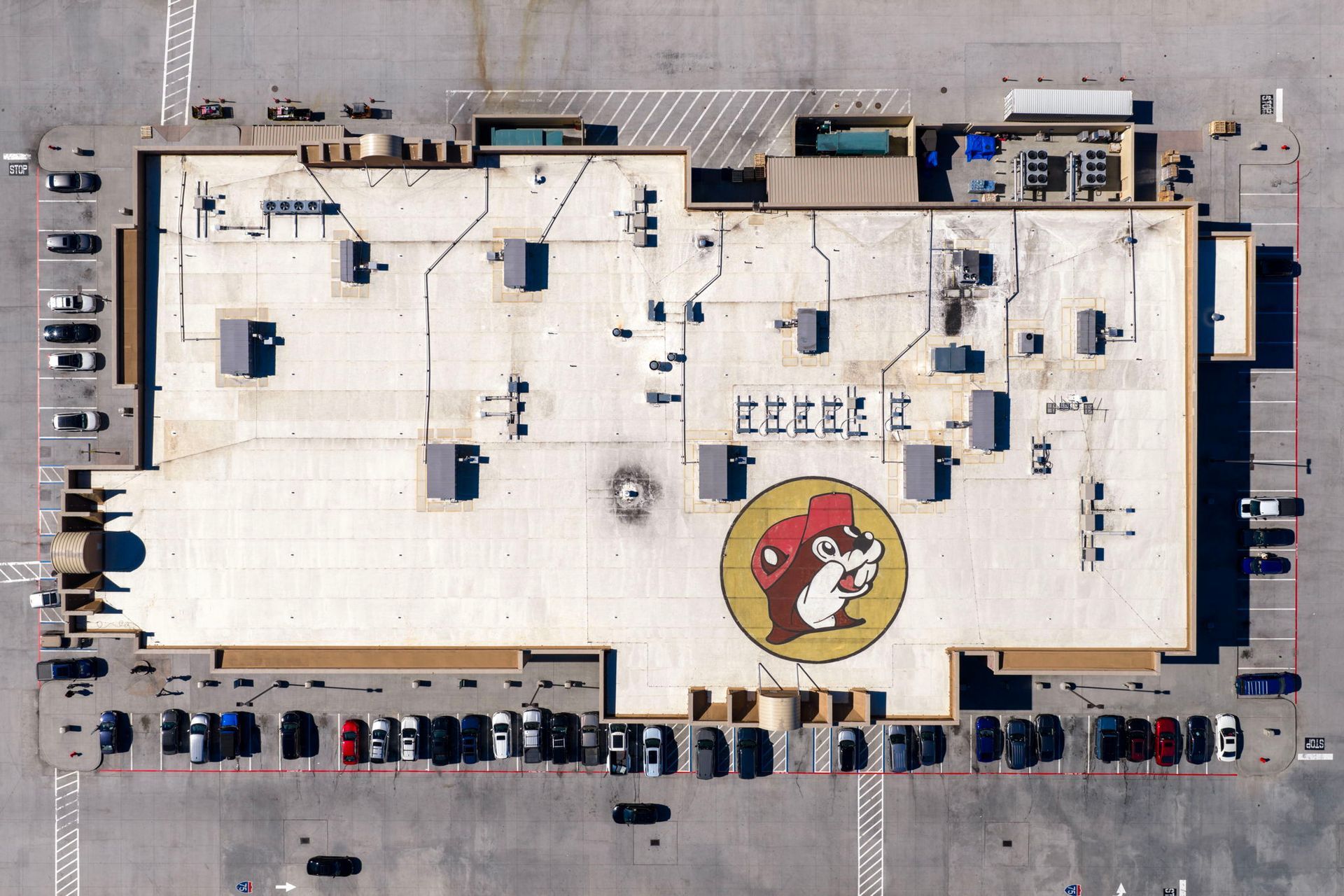 Aerial view of a large flat-roof building with a parking lot and a red circular logo on the roof