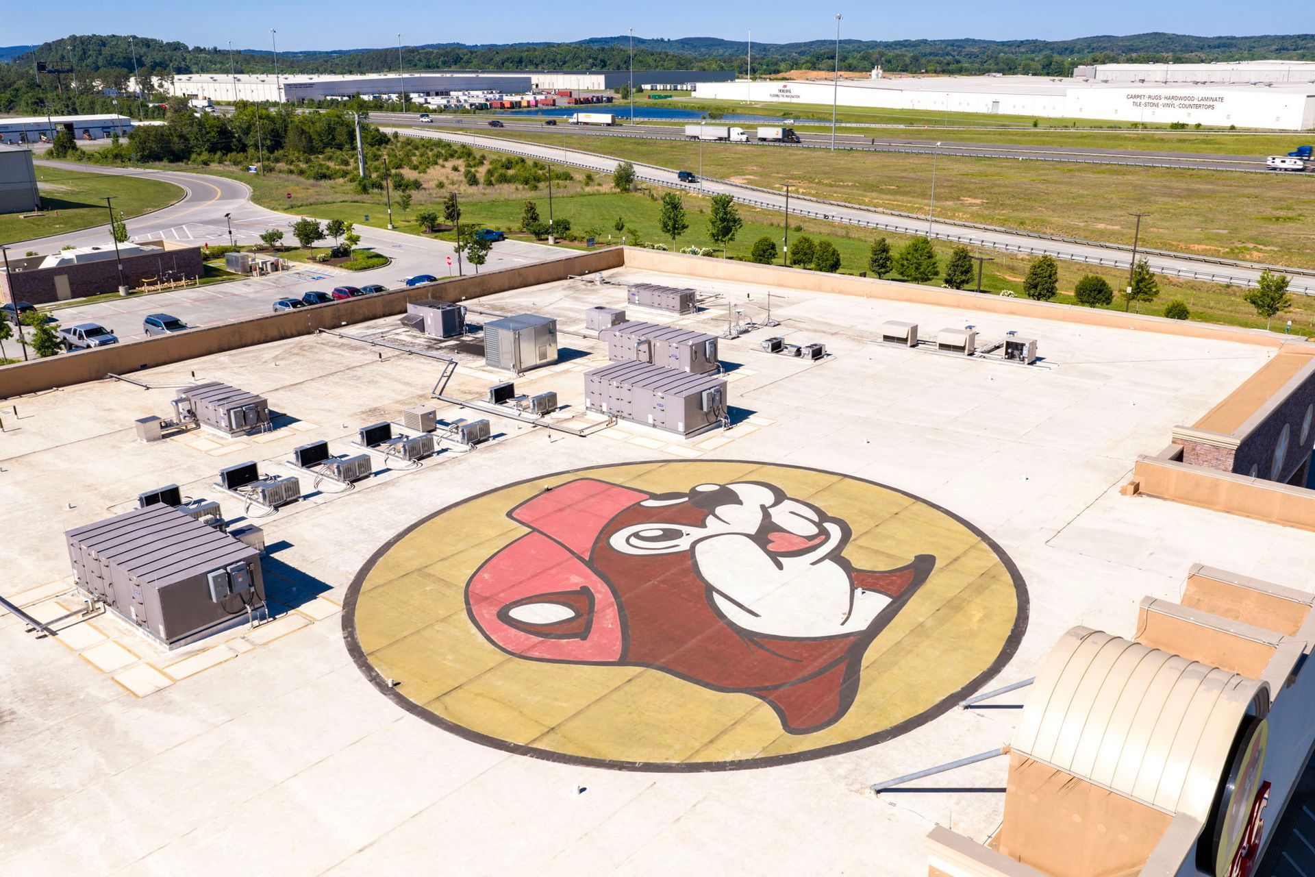 Aerial view of a large factory lot with a huge circular cartoon mural painted on the concrete.