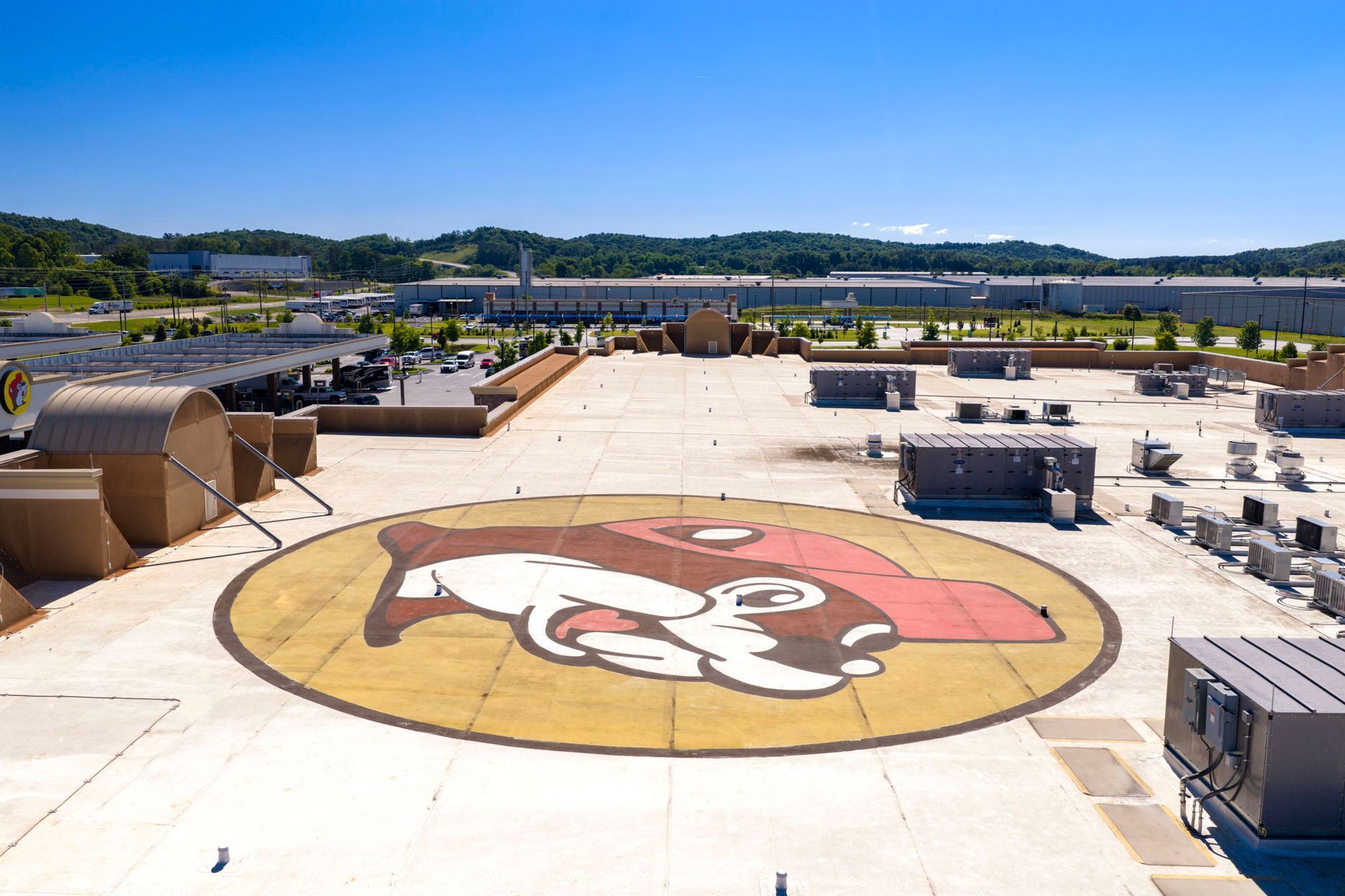 Rooftop with a large painted cartoon face on a concrete helipad, surrounded by equipment and distant hills.