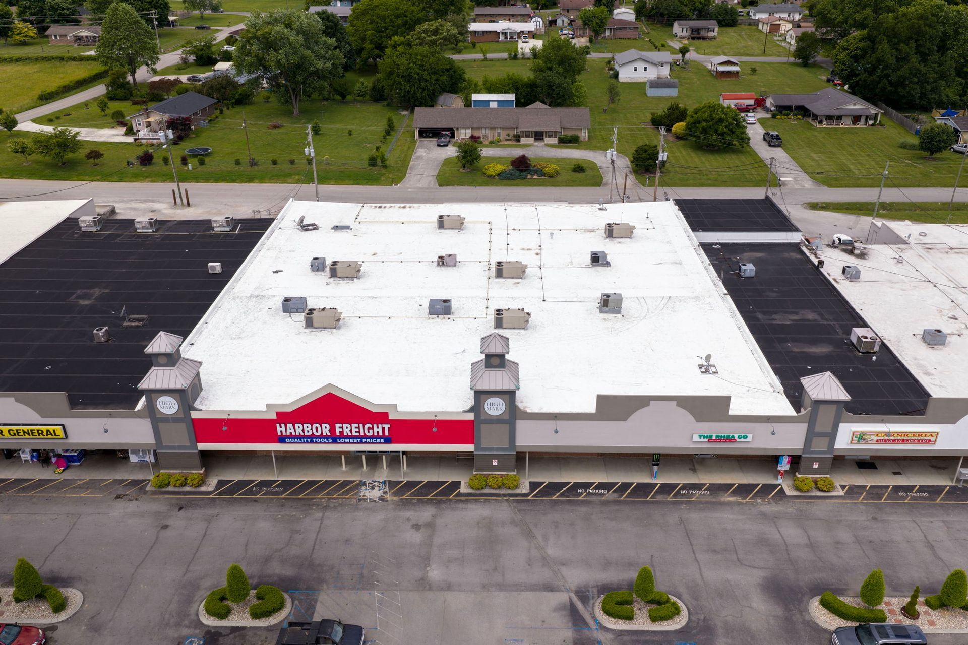 Aerial view of a strip mall with a white roof, red storefront sign, and parking lot in front