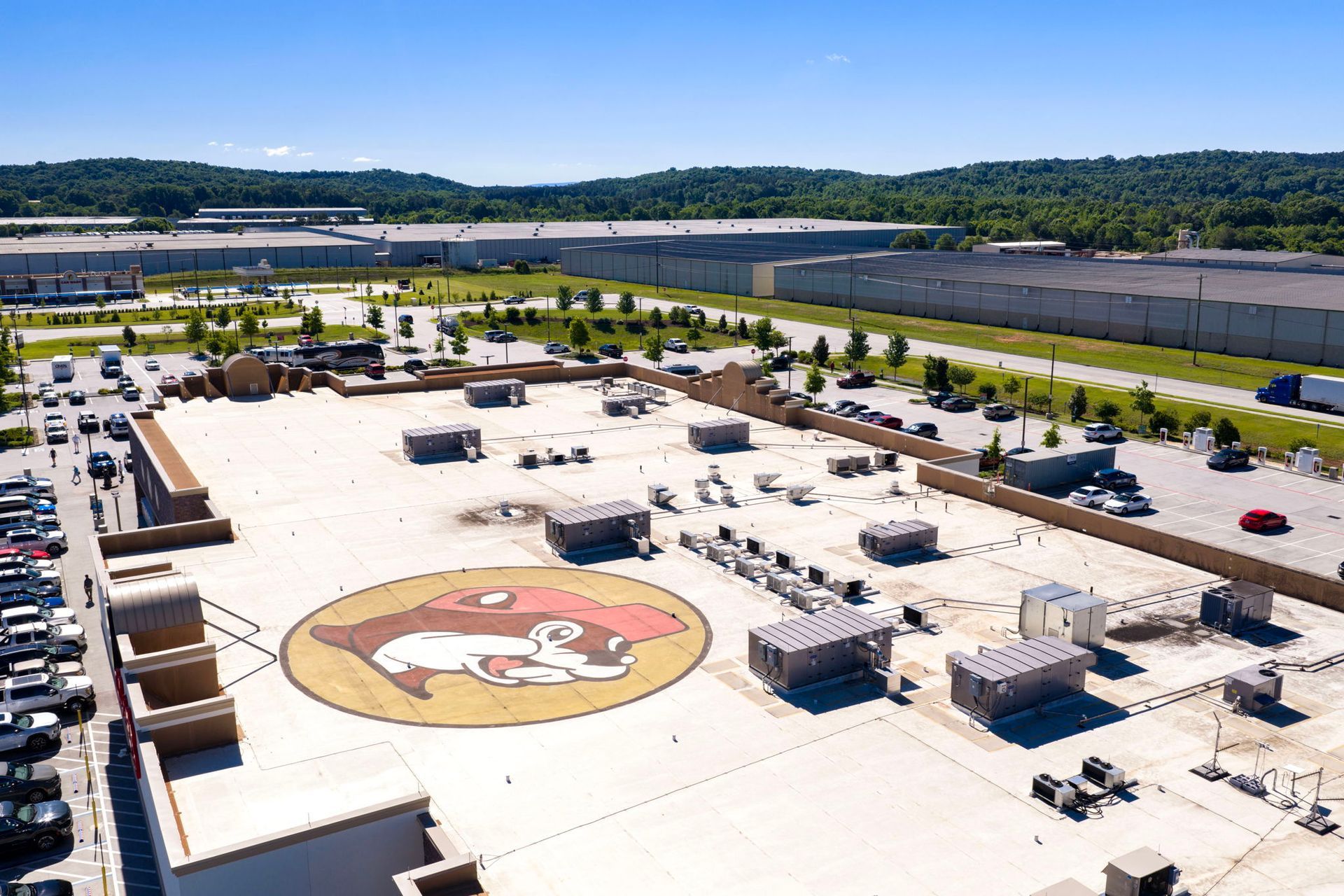 Aerial view of a rooftop parking lot with a large central logo and scattered vehicles near a waterway