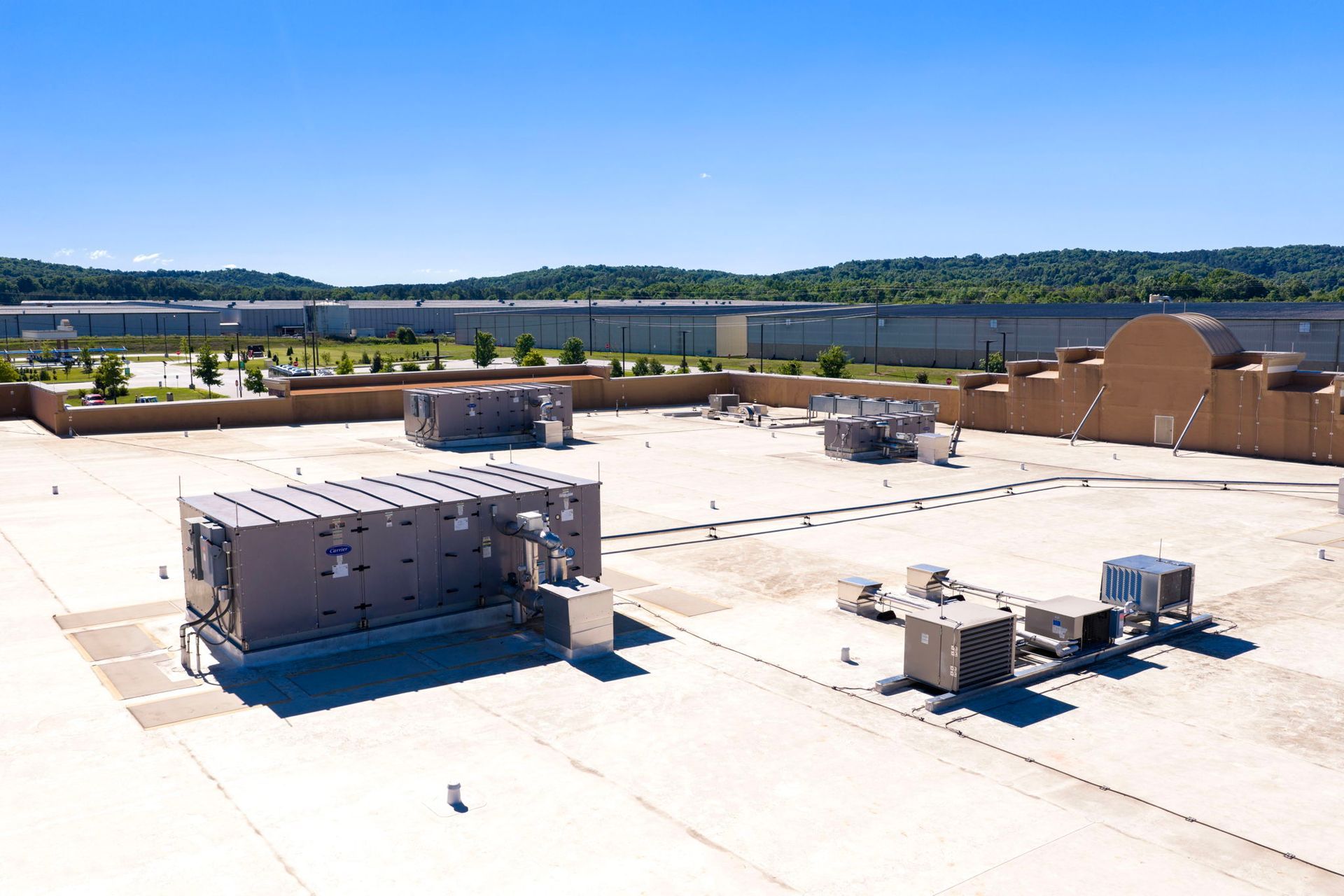 Rooftop HVAC equipment on a flat white roof with trees and water in the background
