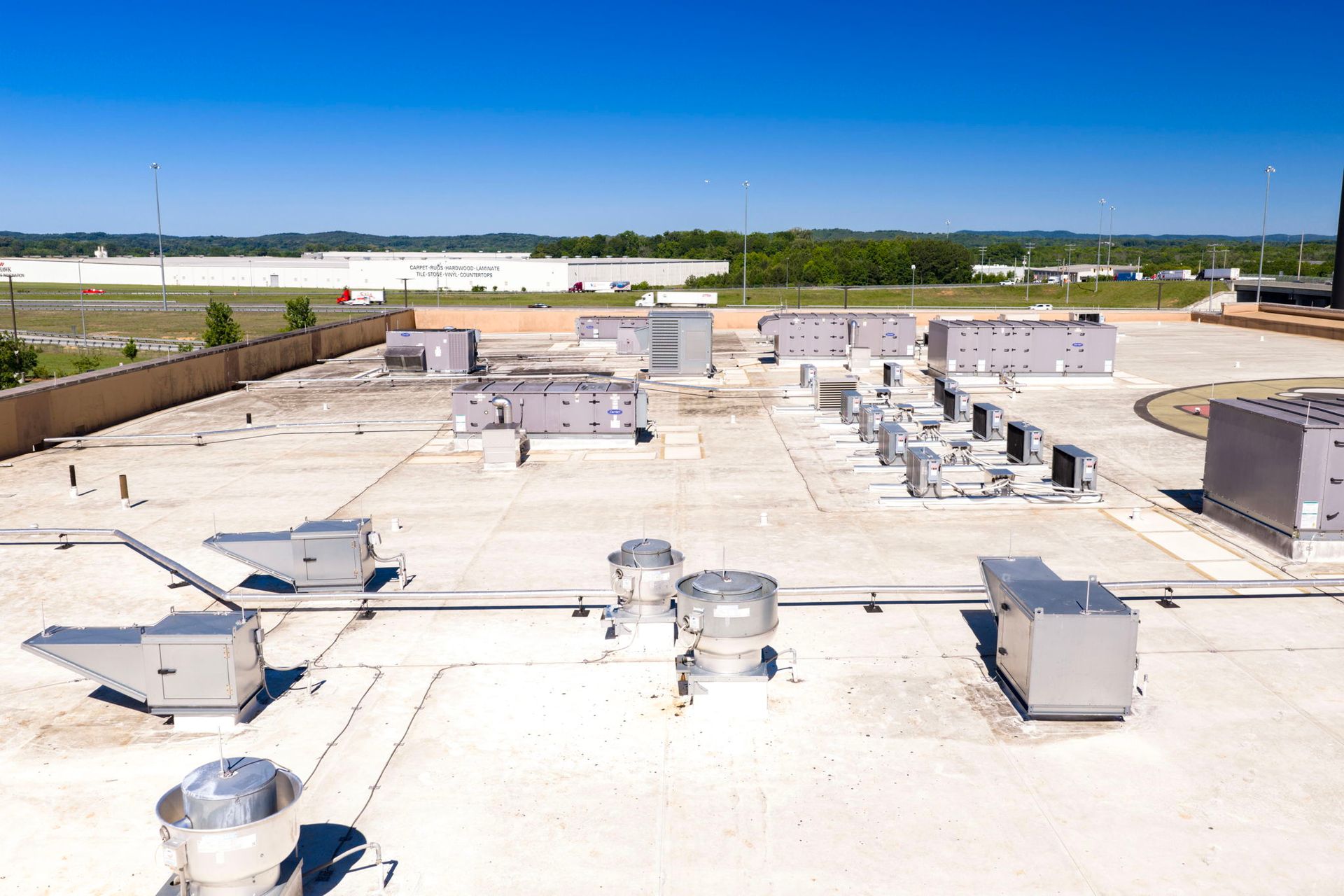 Rooftop with many HVAC units and vents on a flat white industrial roof under a clear blue sky