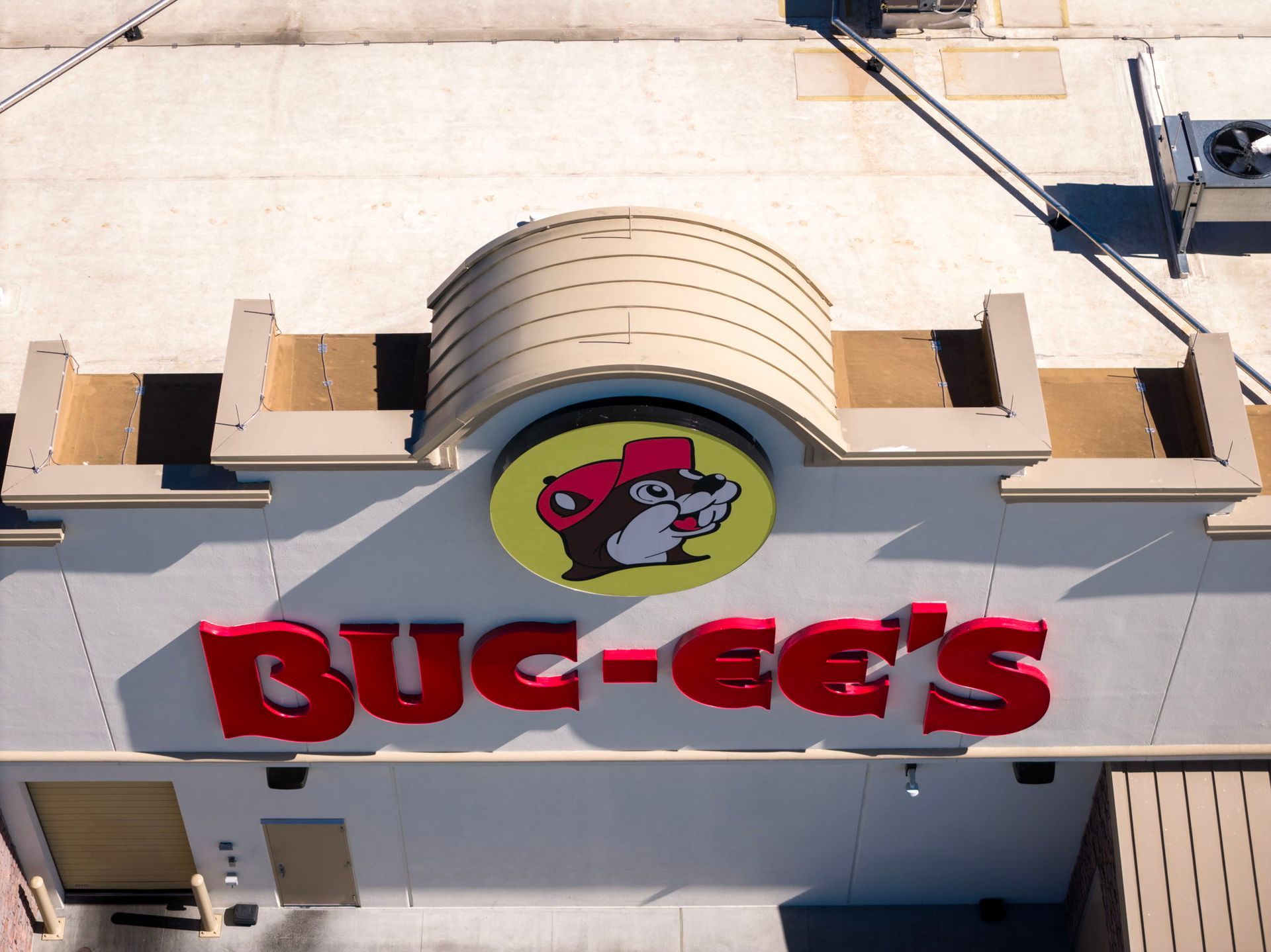 Aerial view of a Buc-ee’s storefront sign with the beaver logo on a beige building