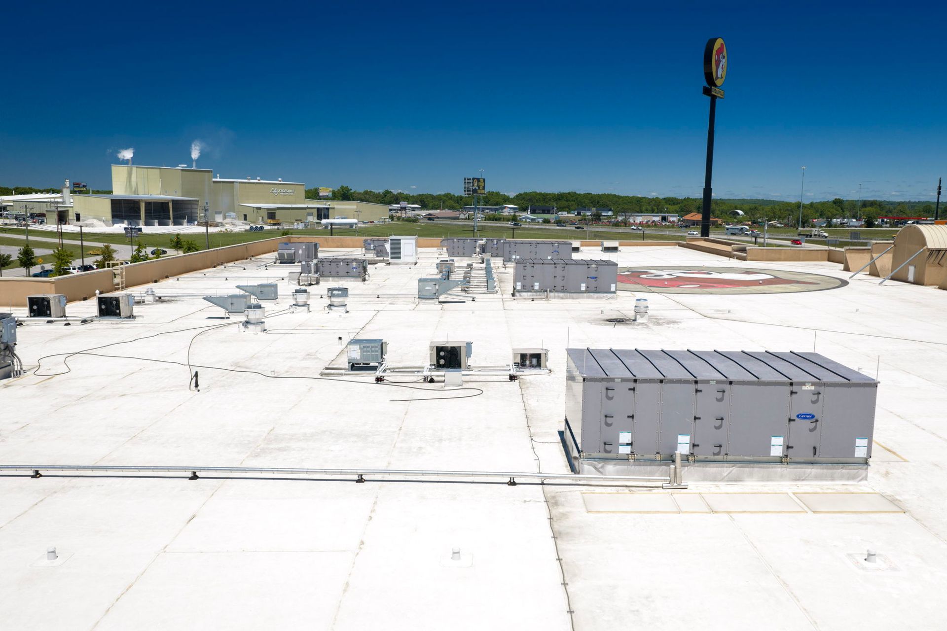 Flat white rooftop with HVAC units under a clear blue sky, viewed from above.