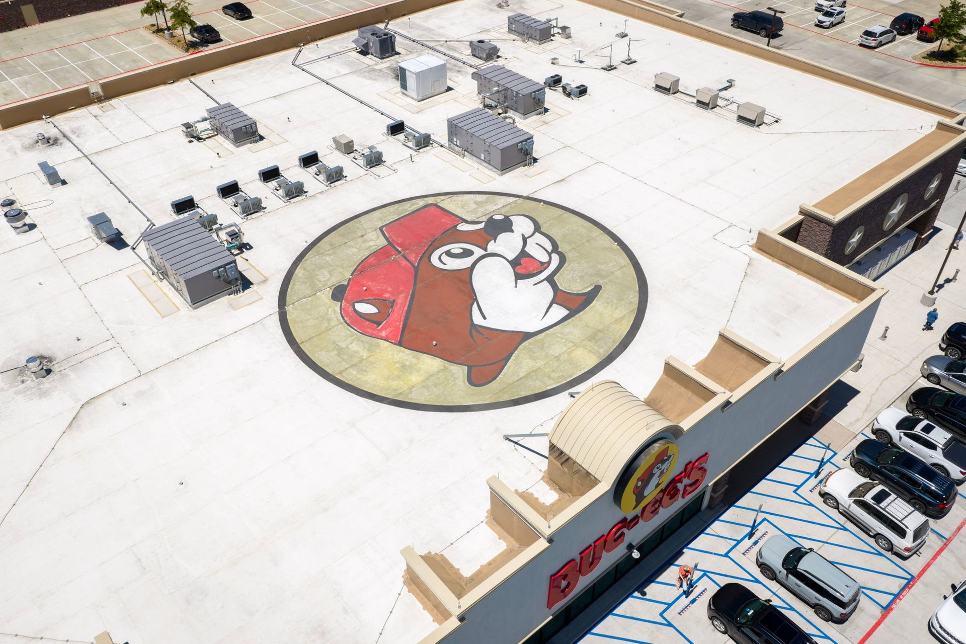 Aerial view of a building rooftop with a large red-and-white cartoon logo mural and parked cars below