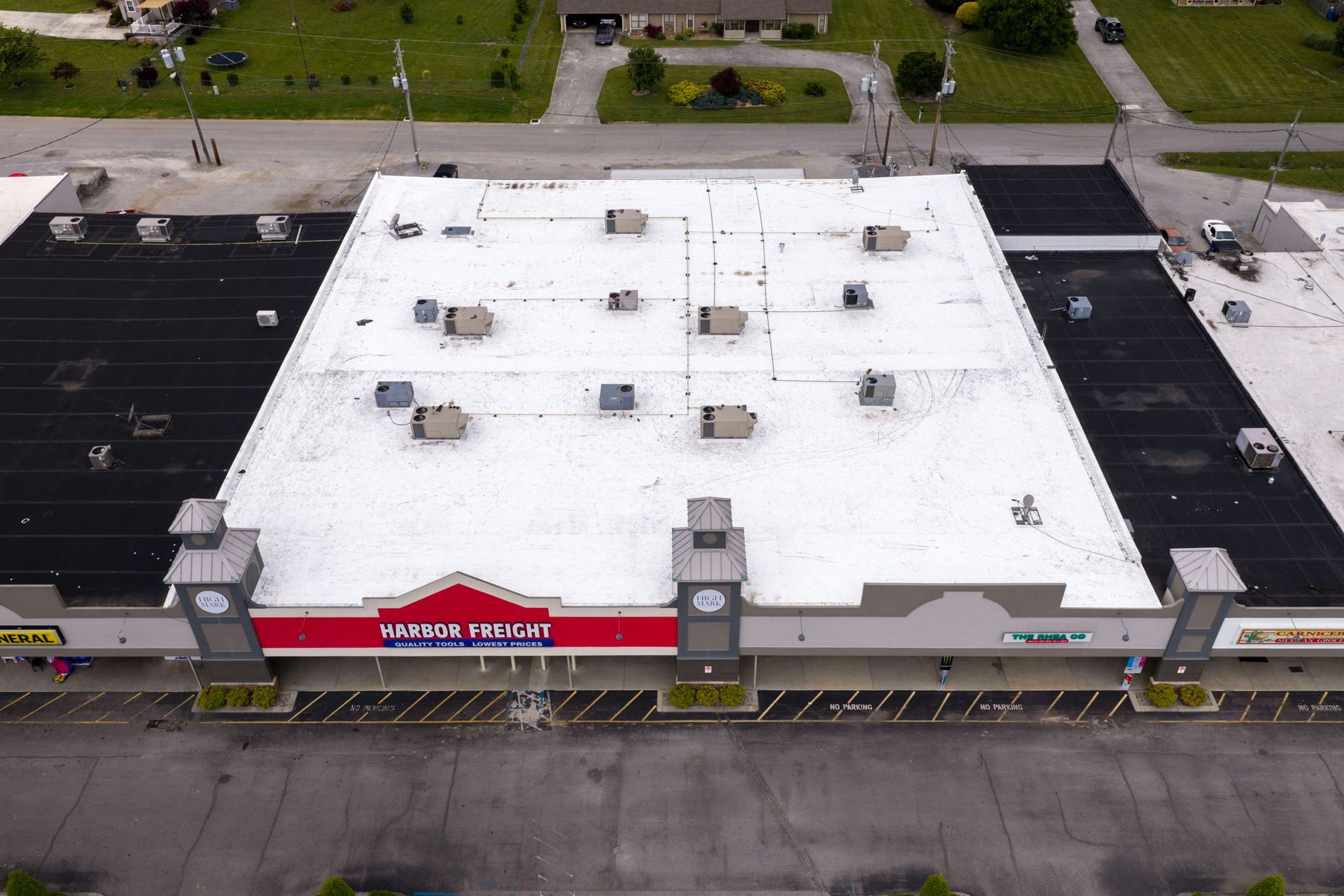 Aerial view of a strip mall with a white roof and red storefront sign