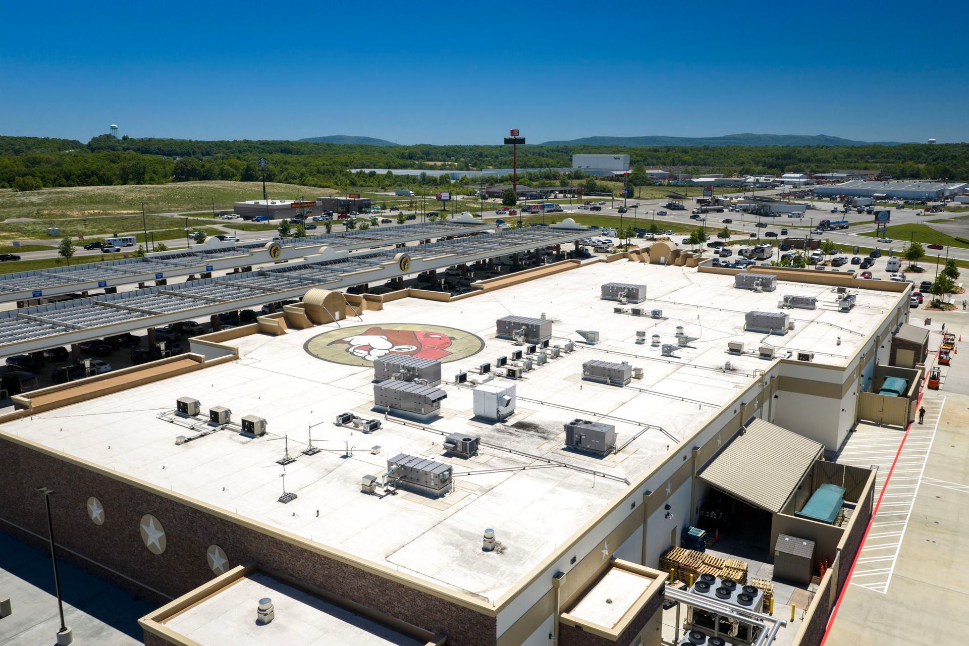 Aerial view of a large flat-roofed commercial building with HVAC units and parking lots under a clear sky