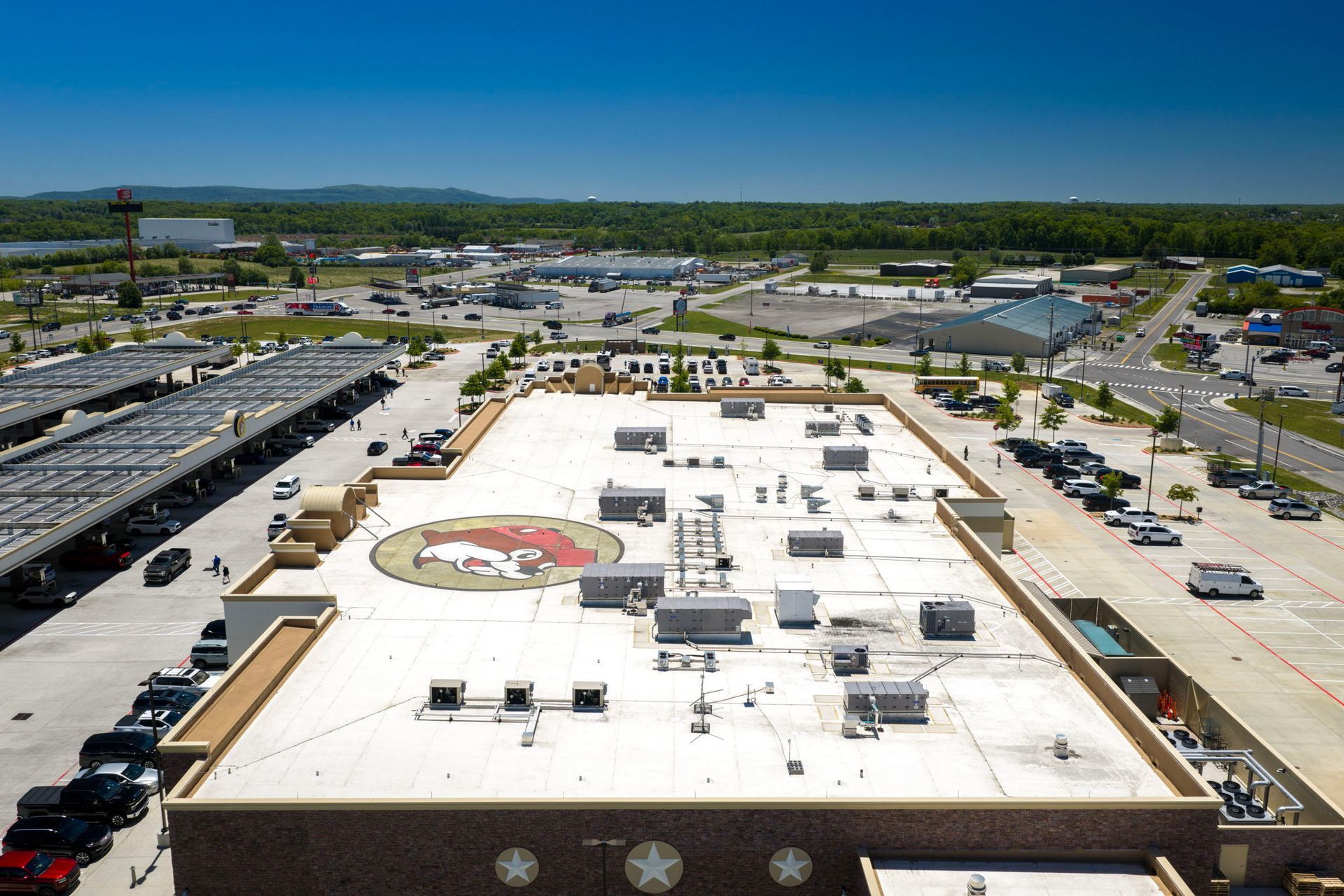 Aerial view of a flat-roof commercial building with parking lots and surrounding roads on a sunny day