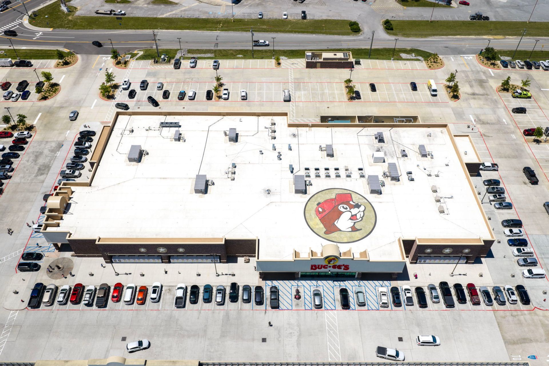 Aerial view of a large white-roofed building with a circular logo and parked cars around it