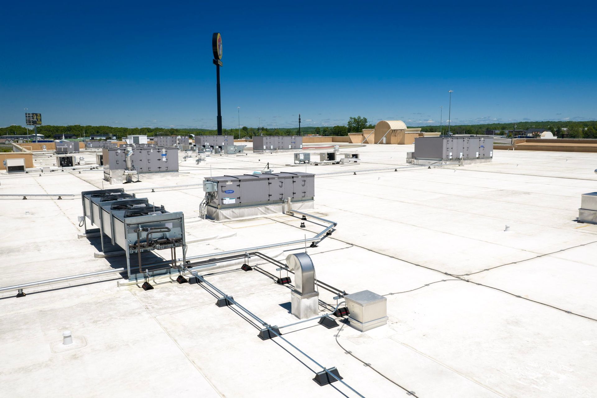 Flat white rooftop with HVAC units, vents, and electrical conduits under a clear blue sky
