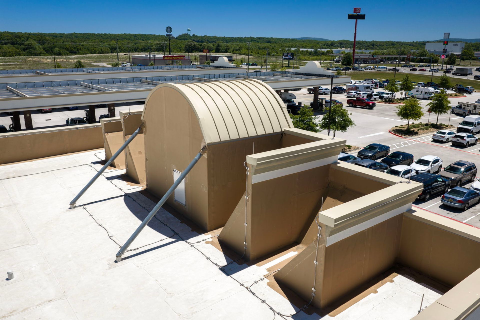 Rooftop HVAC unit with beige ducting above a parking lot and distant roadway under clear skies
