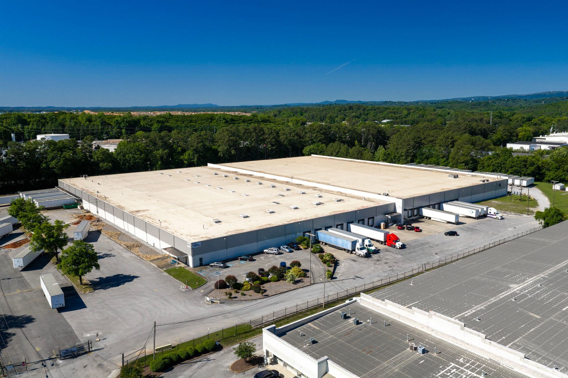 Aerial view of a large beige warehouse with loading docks and trucks in an industrial park