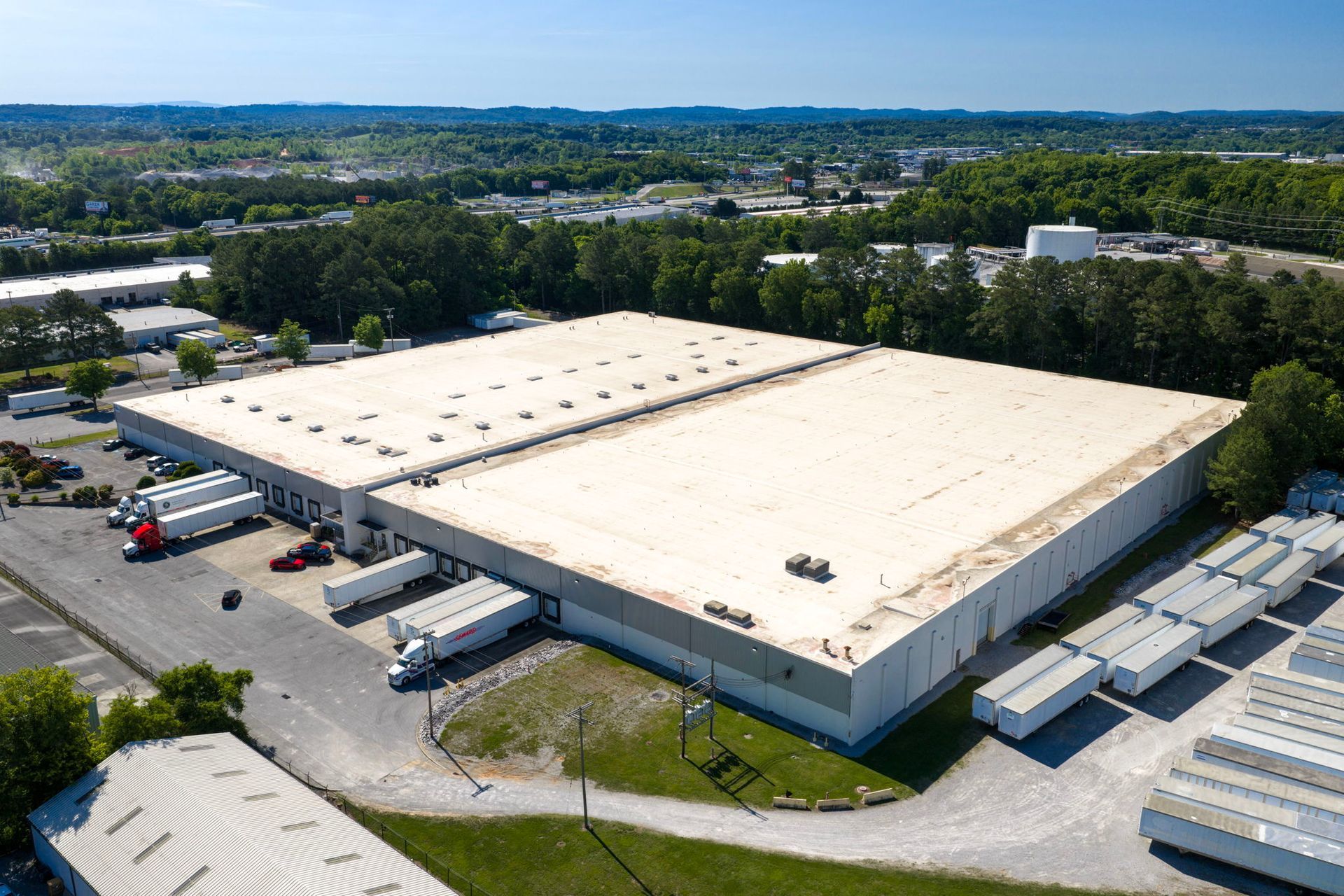 Aerial view of a large white warehouse with loading docks and trucks in an industrial area