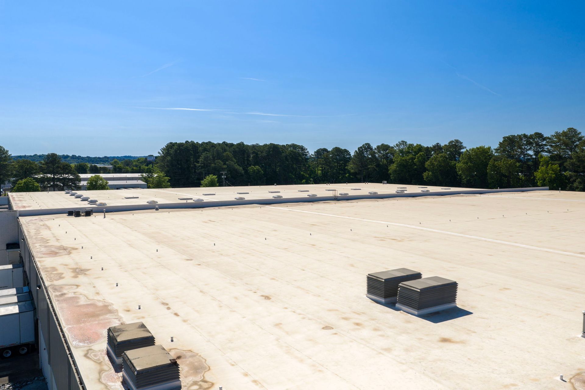 Flat white rooftop with vents under a clear blue sky, trees in the distance